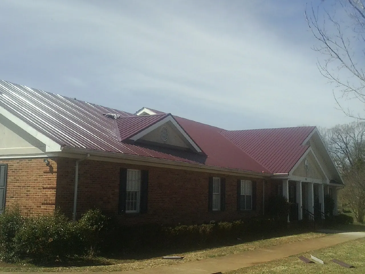 Red metal roof with gabled entries on a long brick building, from a Hail Damage Roof Repair job in Ivanhoe
