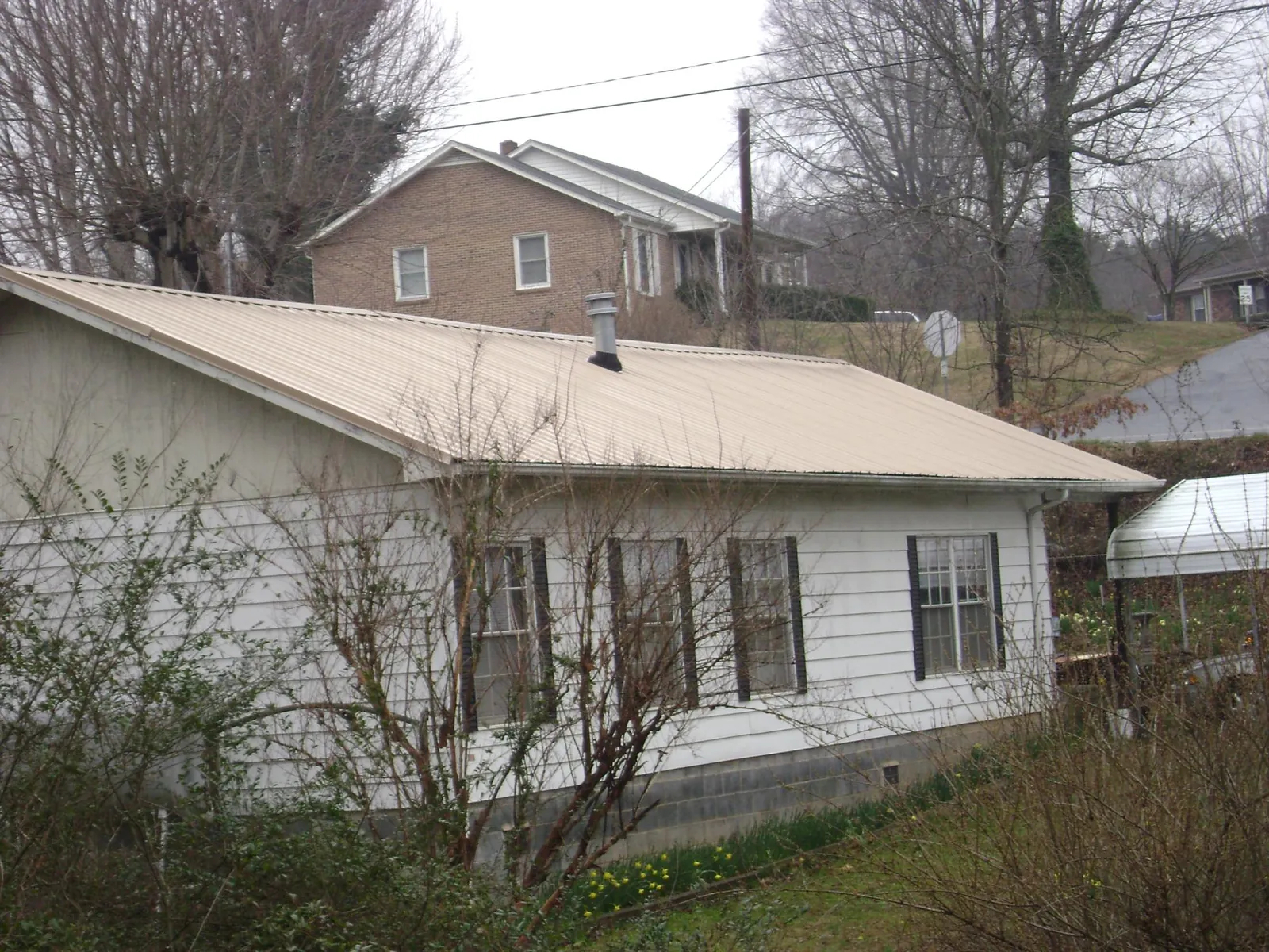 Tan metal roof on a white sided house set into a hillside — Commercial Roofing by Roofing Brothers in Ivanhoe